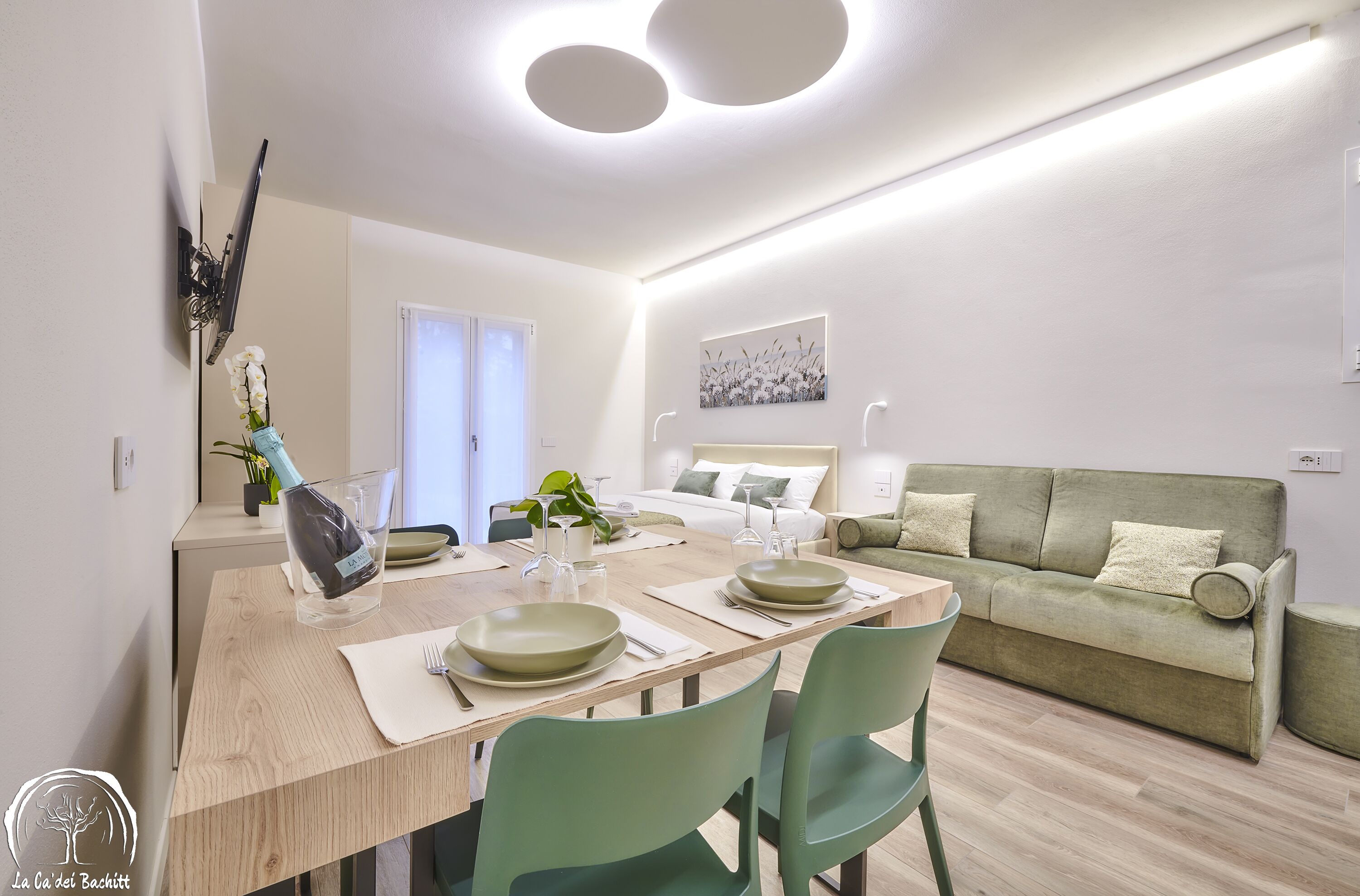 Un comedor moderno con una mesa de madera, sillas verdes y un sofá al fondo.