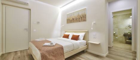 A modern bedroom with a bed, bedside tables, and a bathroom visible through an open door.