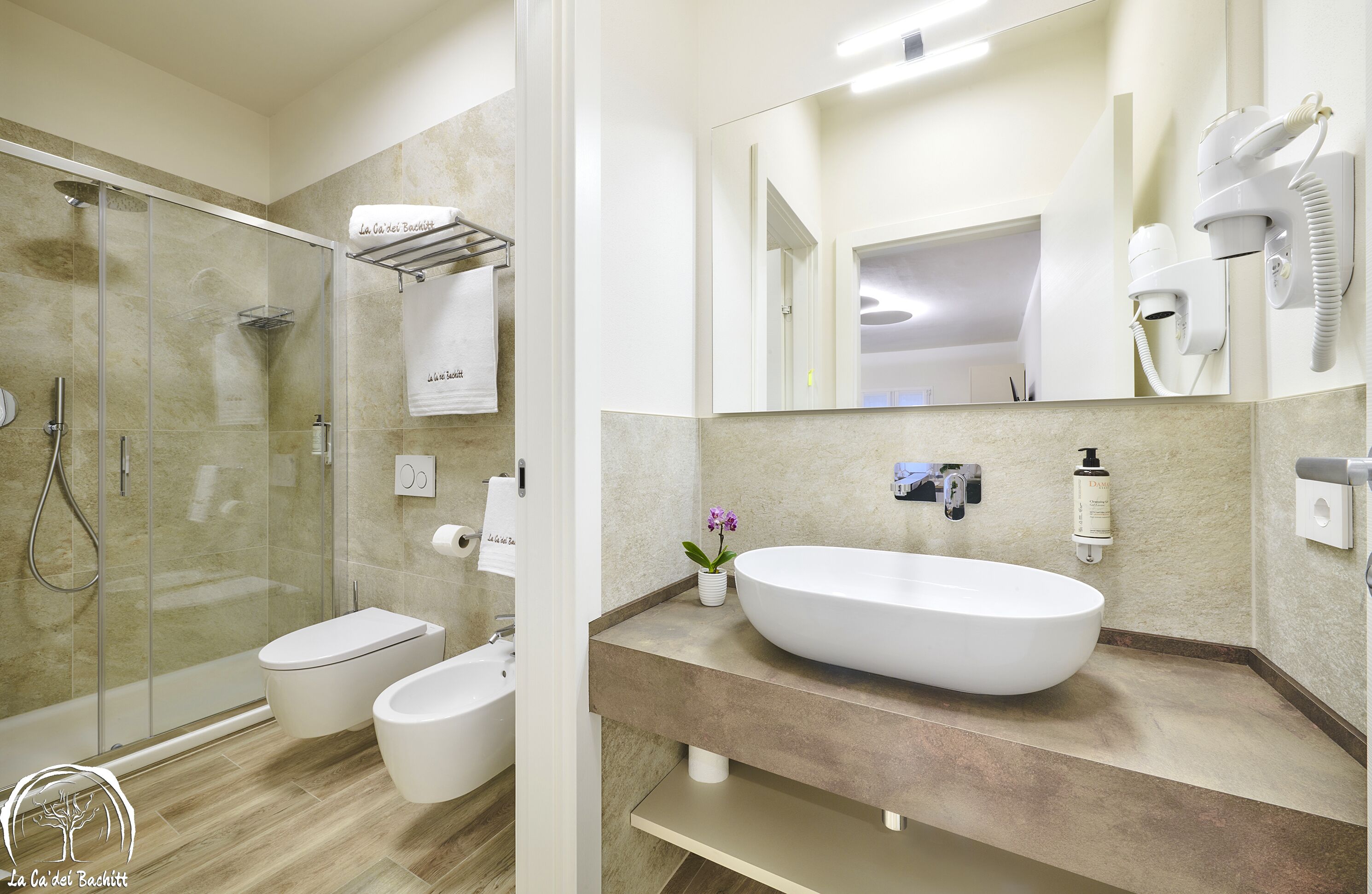 Un baño moderno con ducha de vidrio, lavamanos blanco y un espejo grande.