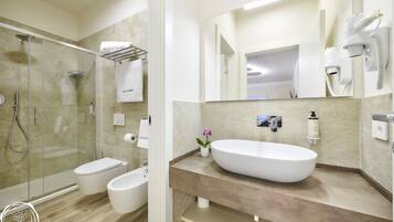 Un baño moderno con ducha de vidrio, lavamanos blanco y un espejo grande.