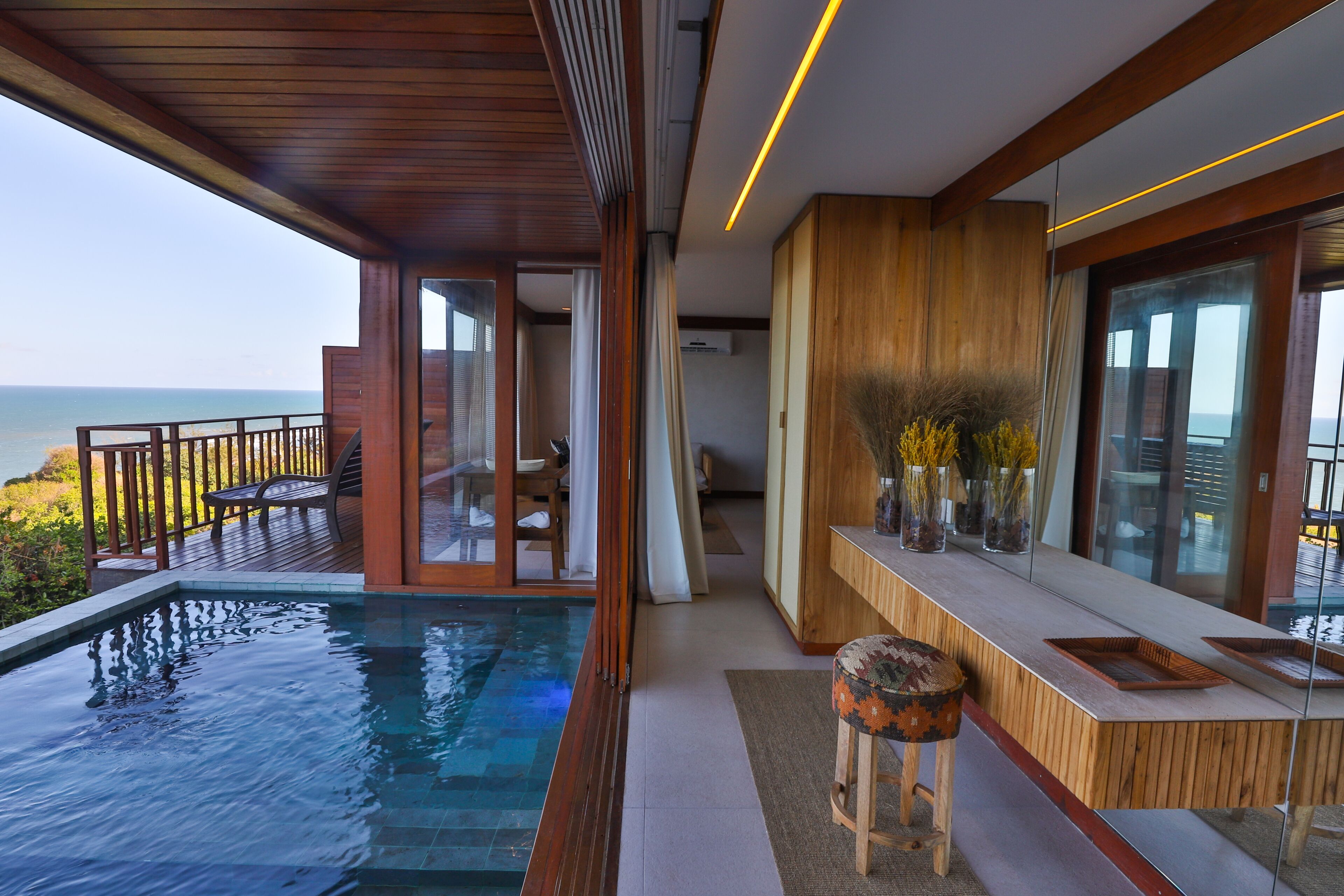 Una piscina infinita moderna con cubierta de madera y balaustrada de vidrio con vistas al mar.