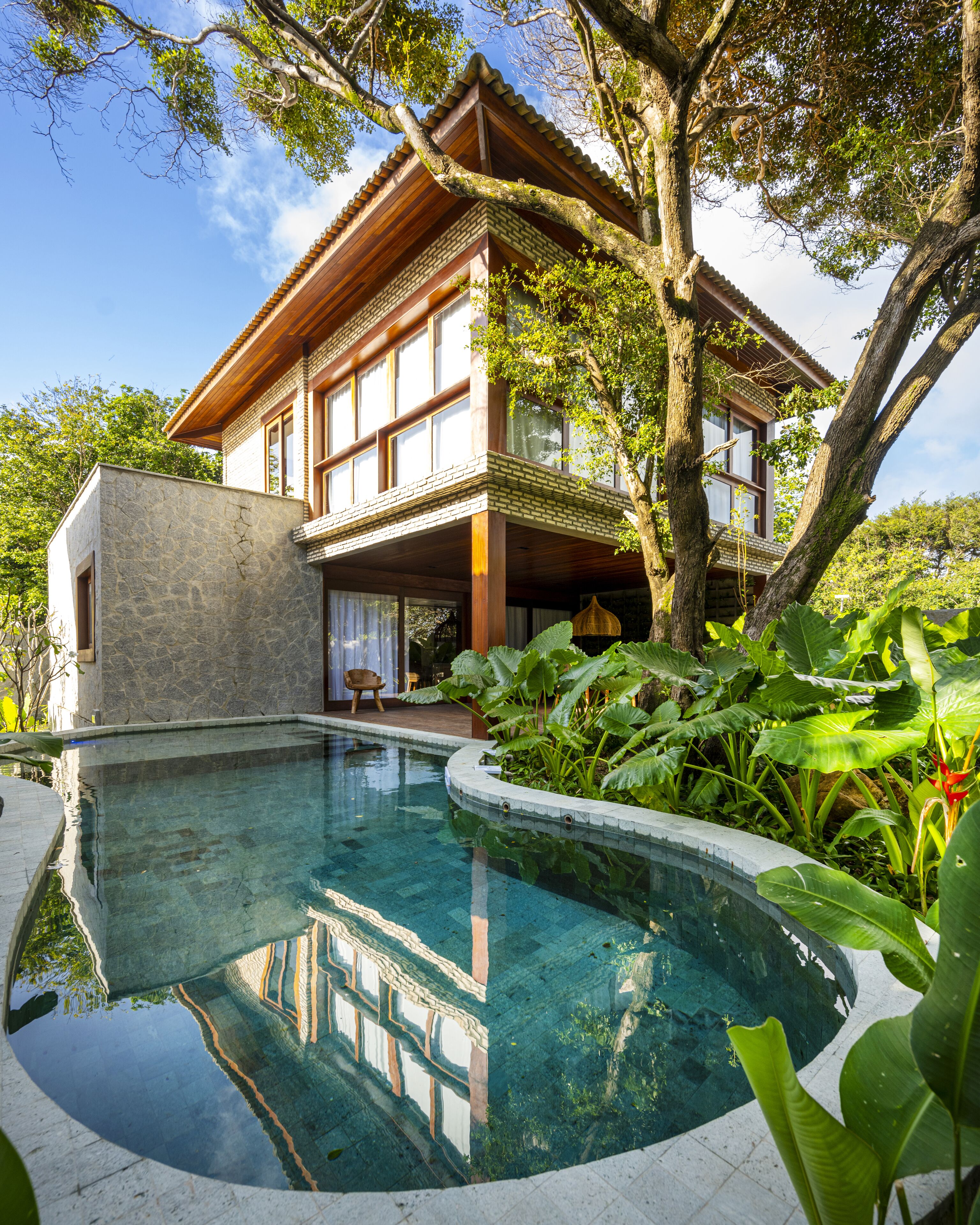 Ein modernes Haus mit Schwimmbad, umgeben von üppiger Vegetation und großen Bäumen.