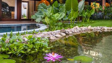 Un edificio moderno con piscina, rodeado de abundante vegetación y un lirio acuático en el agua.