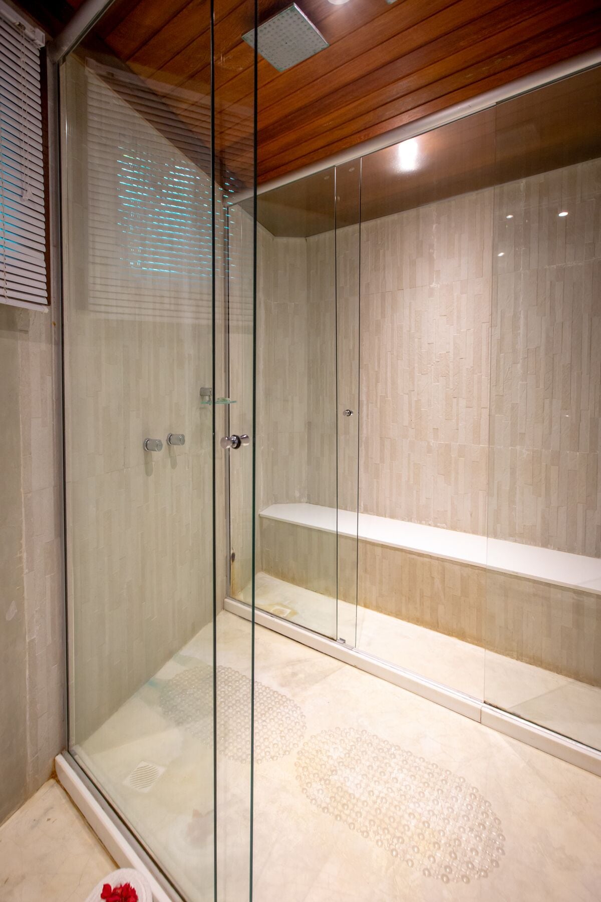 A glass-enclosed shower with a wooden ceiling and tiled walls.