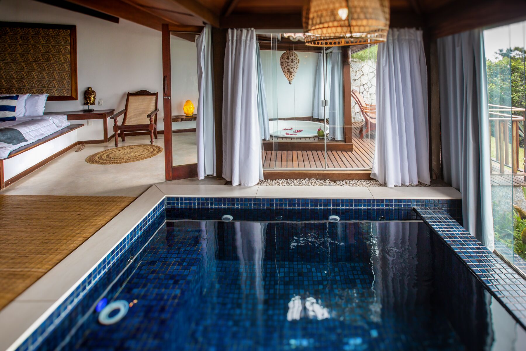 Una habitación de hotel moderna con una amplia piscina de azulejos azules, una terraza de madera y vistas al exterior.