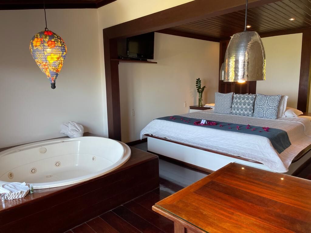 Une chambre à coucher avec un grand lit, une table de chevet en bois, une baignoire blanche et une lanterne suspendue.