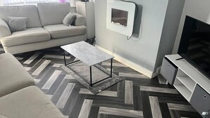 Ett modernt vardagsrum med en soffa, ett soffbord, en tv och ett golv med fiskbensmönster.