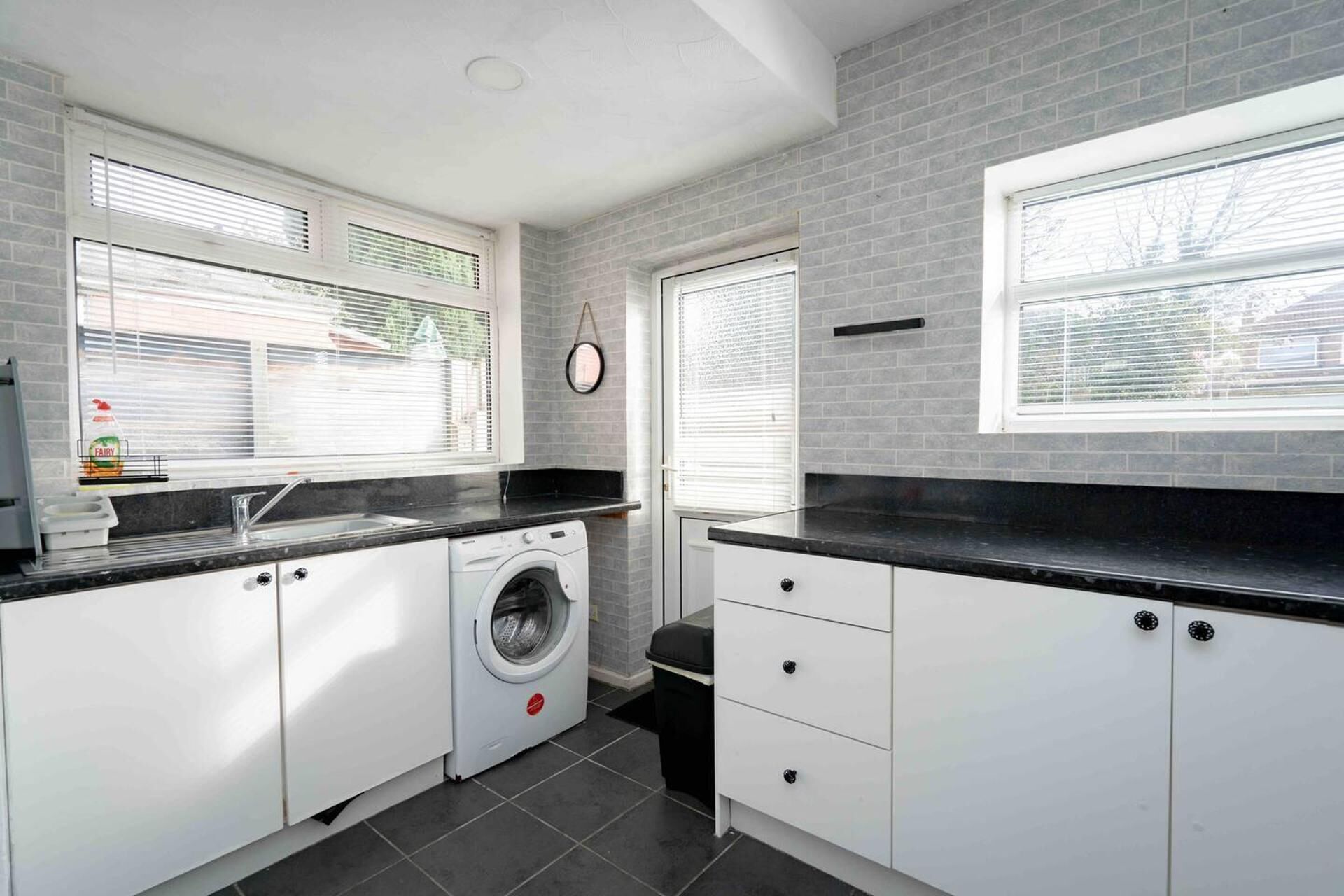 A compact kitchen with a washing machine, a sink, and a window with blinds.