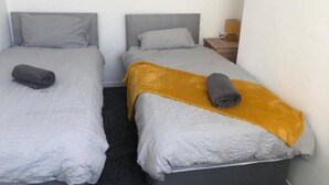 A small, clean room with two single beds, each with a pillow and a rolled towel.