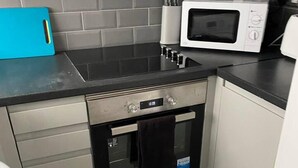 A compact kitchen with a built-in oven, a microwave, and a blue cutting board on the countertop.