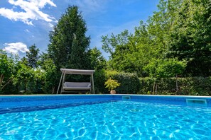 A clear blue swimming pool with a white canopy and a potted plant nearby.