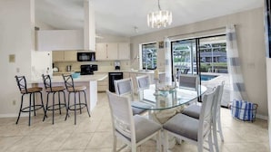 A modern kitchen with white cabinets, a black microwave, and a glass dining table with white chairs. - Welcome to Villa Ibis Cozy Directly on the Water (Cape Coral)