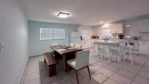A modern kitchen with white cabinets, a central island, and a dining area with a wooden table and chairs.
