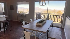 A dining area with a table and chairs, a small kitchen area, and a balcony with a view of the landscape.