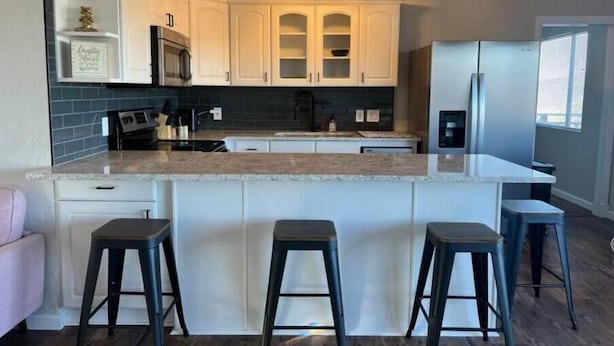 A modern kitchen with white cabinetry, a granite countertop, and a central island with bar stools.