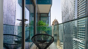Ein moderner Balkon mit Glastrennstäben, schwarzen Gestellstühlen und Blick auf umliegende Hochhäuser.