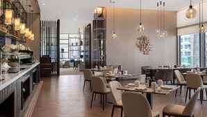 Ein modernes Restaurant mit Holzböden, mehreren Esstischen und zeitgemäßen Leuchten.