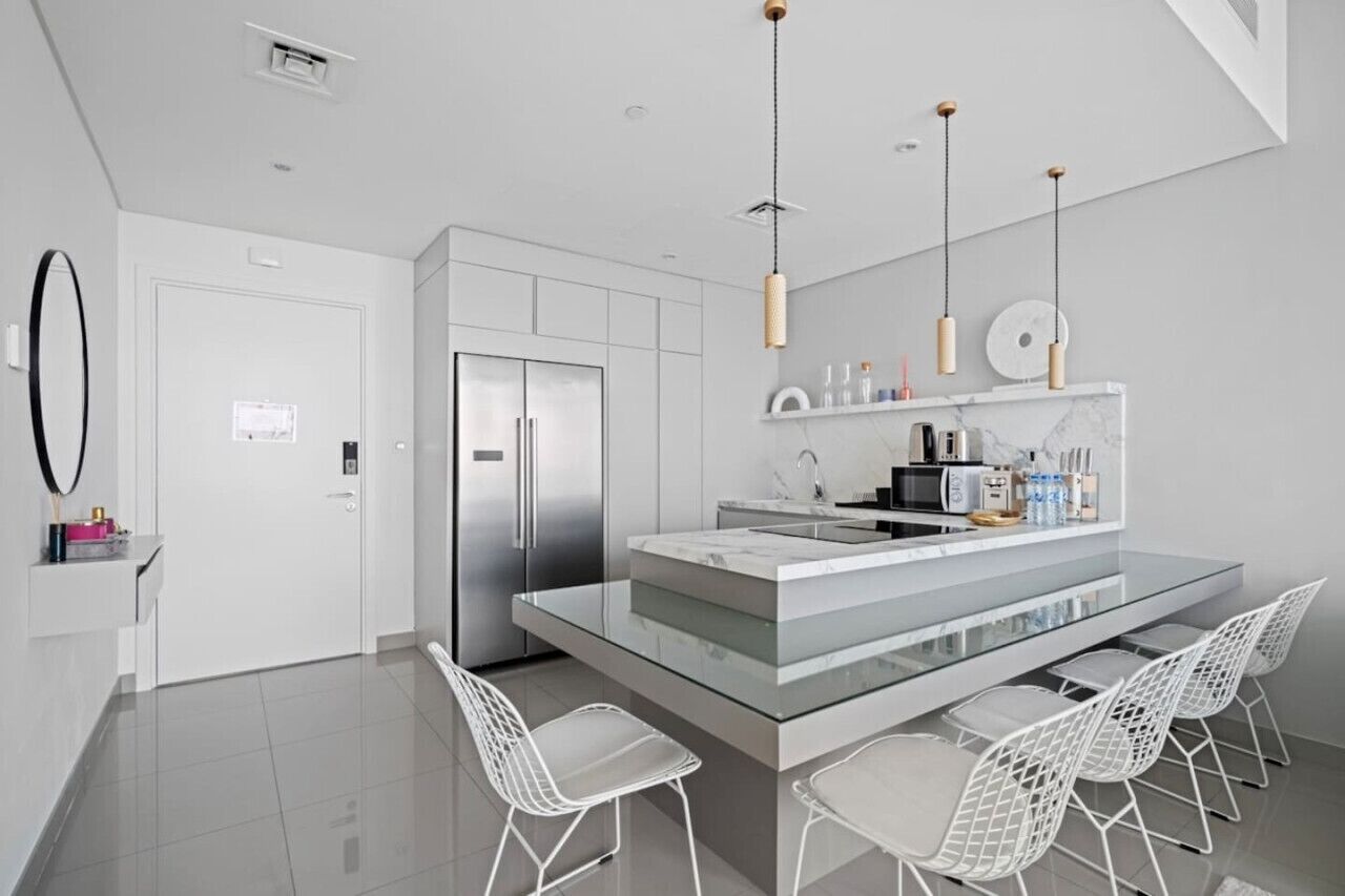 A modern kitchen with a central island, white chairs, and pendant lighting.