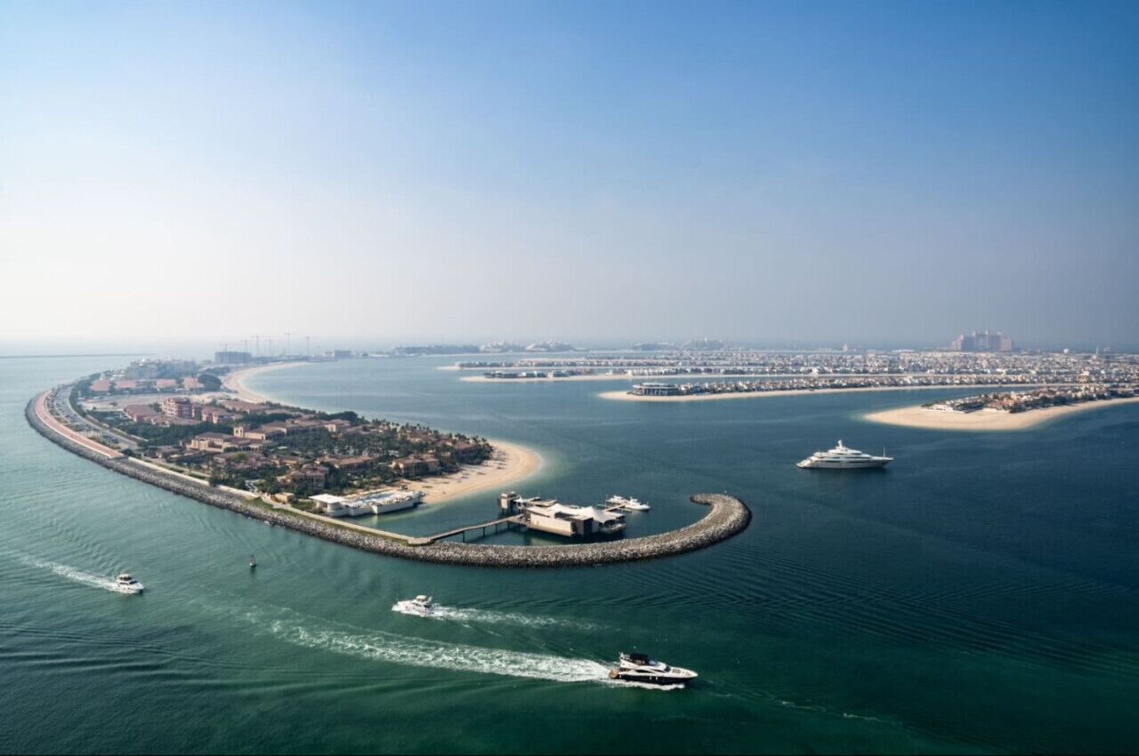 An aerial view of a coastal city with a marina, several islands, and a large cruise ship.
