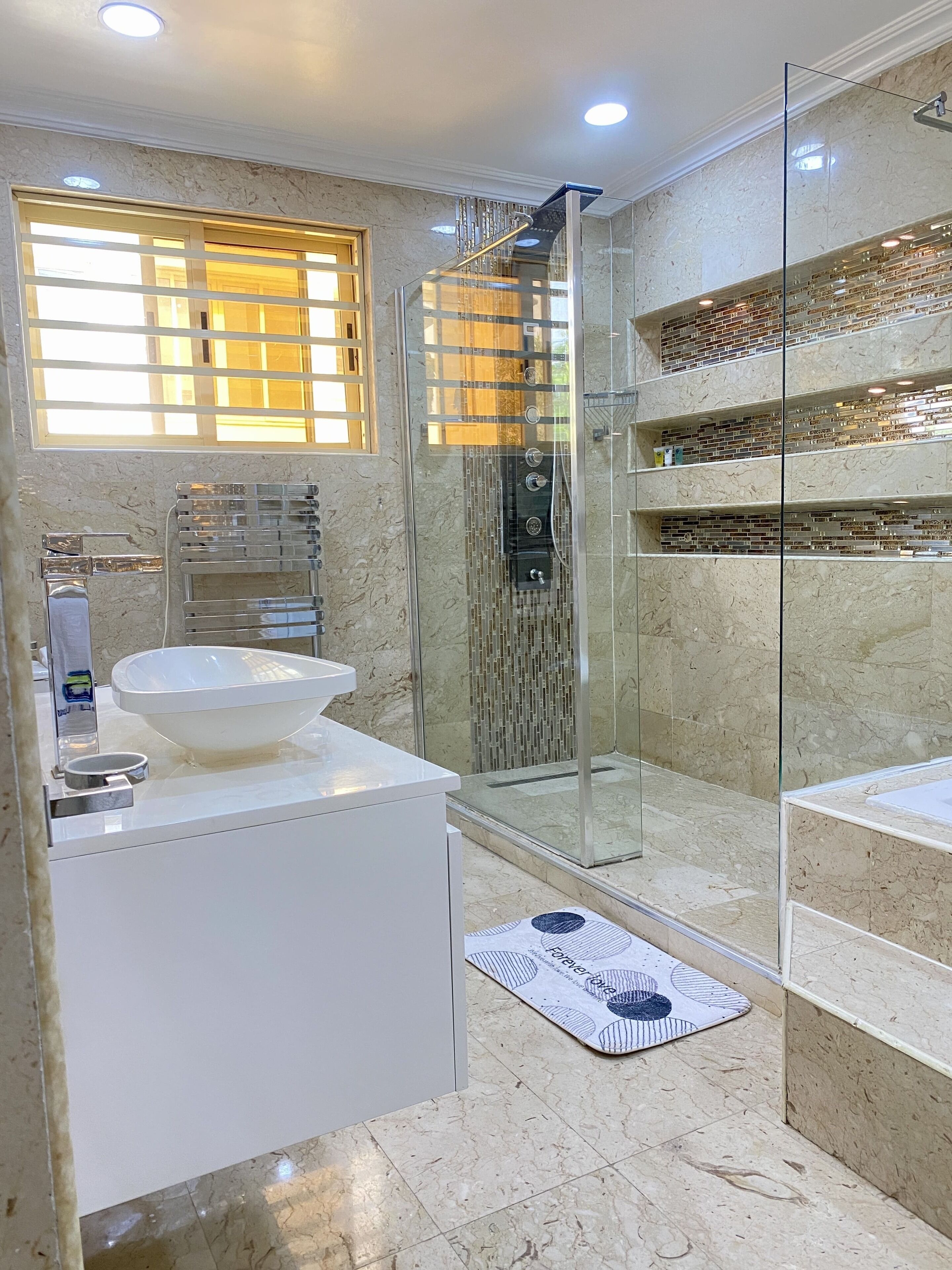 A modern bathroom with a glass-enclosed shower, a white sink, and a marble floor.