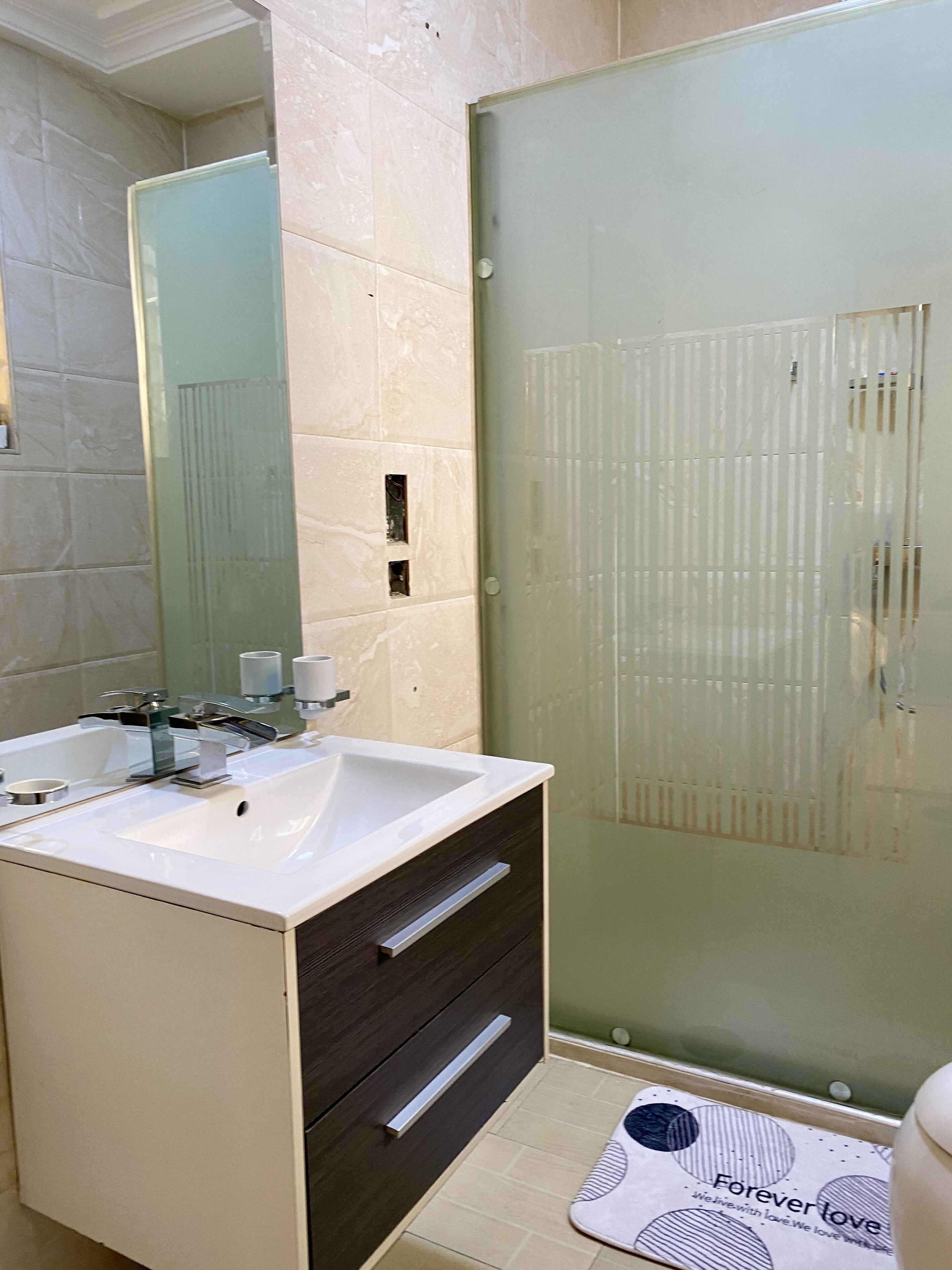 A modern bathroom with a white sink, dark wooden cabinet, and a glass shower enclosure.