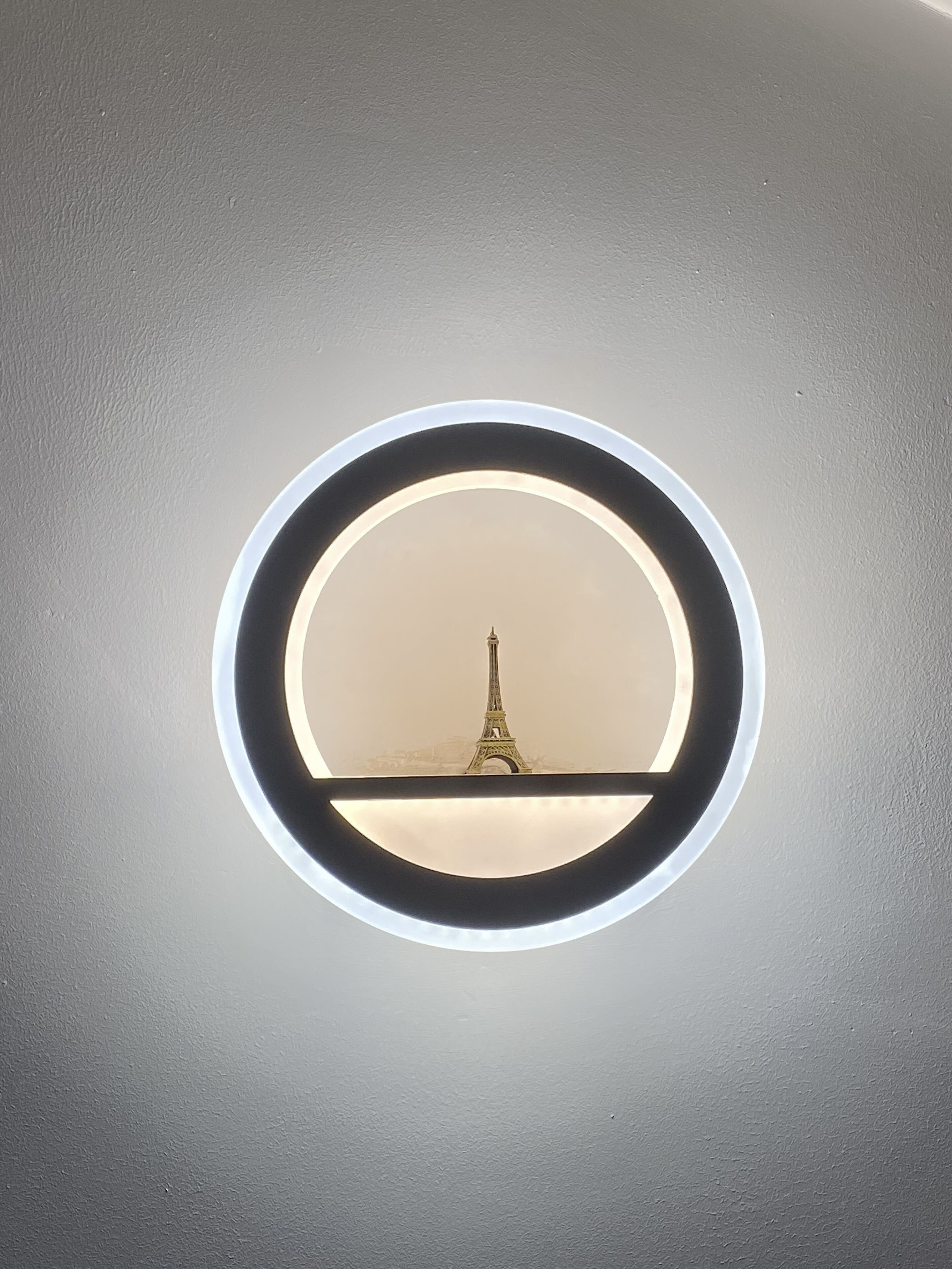 A circular light fixture with a view of the Eiffel Tower through a clear glass panel.