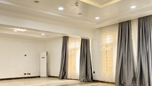 A spacious room with a marble floor, large windows with grey curtains, and recessed ceiling lighting. - Glovis Luxury Apartments (Abuja)
