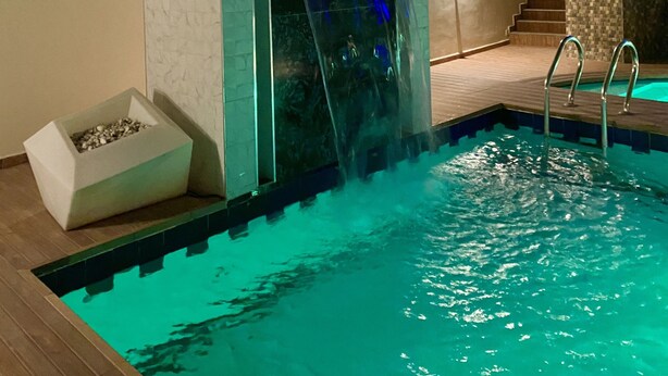 A swimming pool with a waterfall feature, surrounded by a stone wall and a wooden deck. - Glovis Luxury Apartments (Abuja)