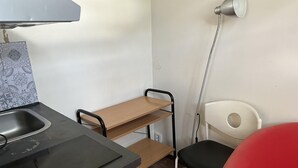 A kitchenette with a sink, a wooden shelf, a chair, and a red chair.