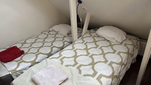A small, single-room accommodation with two beds, each with a patterned bedspread and pillows.