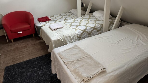 A small, cozy room with two beds, a red chair, and a skylight.