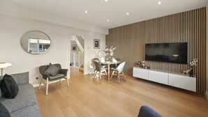 Ein modernes Wohnzimmer mit Essbereich, einer Treppe und einem an einer Holzvertäfelung befestigten Fernseher.
