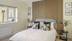Ein Schlafzimmer mit einem großen Bett, einem Fenster mit Blick auf ein Ziegelgebäude, einem Heizkörper und einer Wand mit vertikalen Holzleisten.