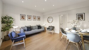 Ein modernes Wohnzimmer mit grauem Sofa, blauem Sessel und Esstisch für vier Personen.