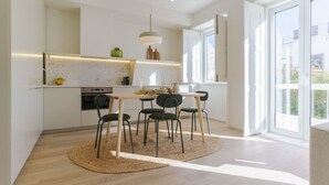Eine moderne Küche mit weißen Schränken, einer Marmor-Spritzschutzwand und einem Essbereich mit einem runden Teppich und vier Stühlen.