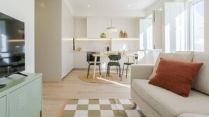 Ein modernes Wohnzimmer mit Sofa, Fernseher und einer Küche im Hintergrund.