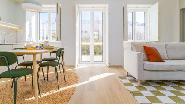 Ein helles Wohnzimmer mit einer Couch, einem Esstisch mit Stühlen und einem großen Fenster.