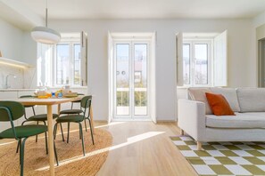 A bright living room with a sofa, a dining table with chairs, and a large window. - Modern & Bright Faro Mercado Apt 12 by Lisbeyond (Faro)