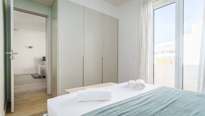 A hotel room with a bed, a wooden nightstand, a large wardrobe, and a view through a sliding glass door. - Modern & Cozy Faro Mercado Apt 21 by Lisbeyond (Faro)