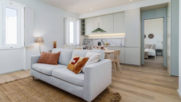 A modern apartment with a light grey sofa, a kitchen with white cabinets, and a dining area. - Modern & Cozy Faro Mercado Apt 21 by Lisbeyond (Faro)