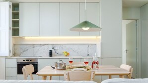 A modern kitchen with white cabinets, a marble countertop, a dining table with chairs, and a hanging light fixture. - Modern & Cozy Faro Mercado Apt 21 by Lisbeyond (Faro)