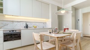 A modern kitchen with white cabinets, a built-in oven, and a dining table with four chairs. - Modern & Cozy Faro Mercado Apt 21 by Lisbeyond (Faro)