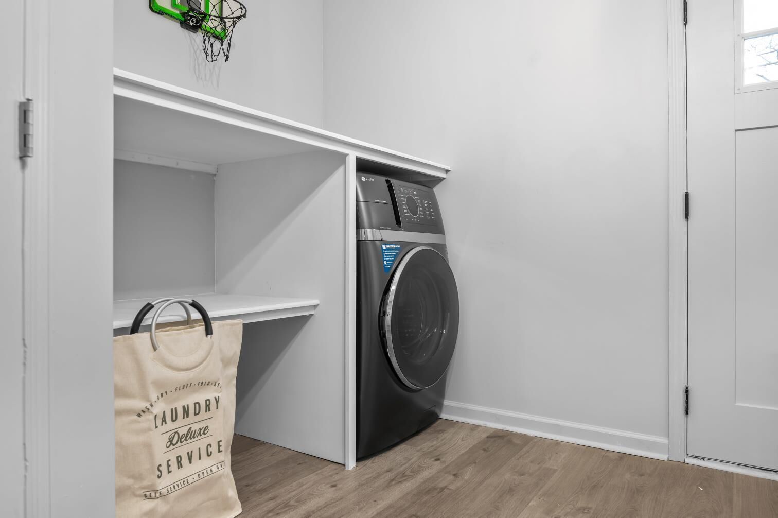 A laundry room with a washing machine, a drying rack, and a bag labeled "laundry service."