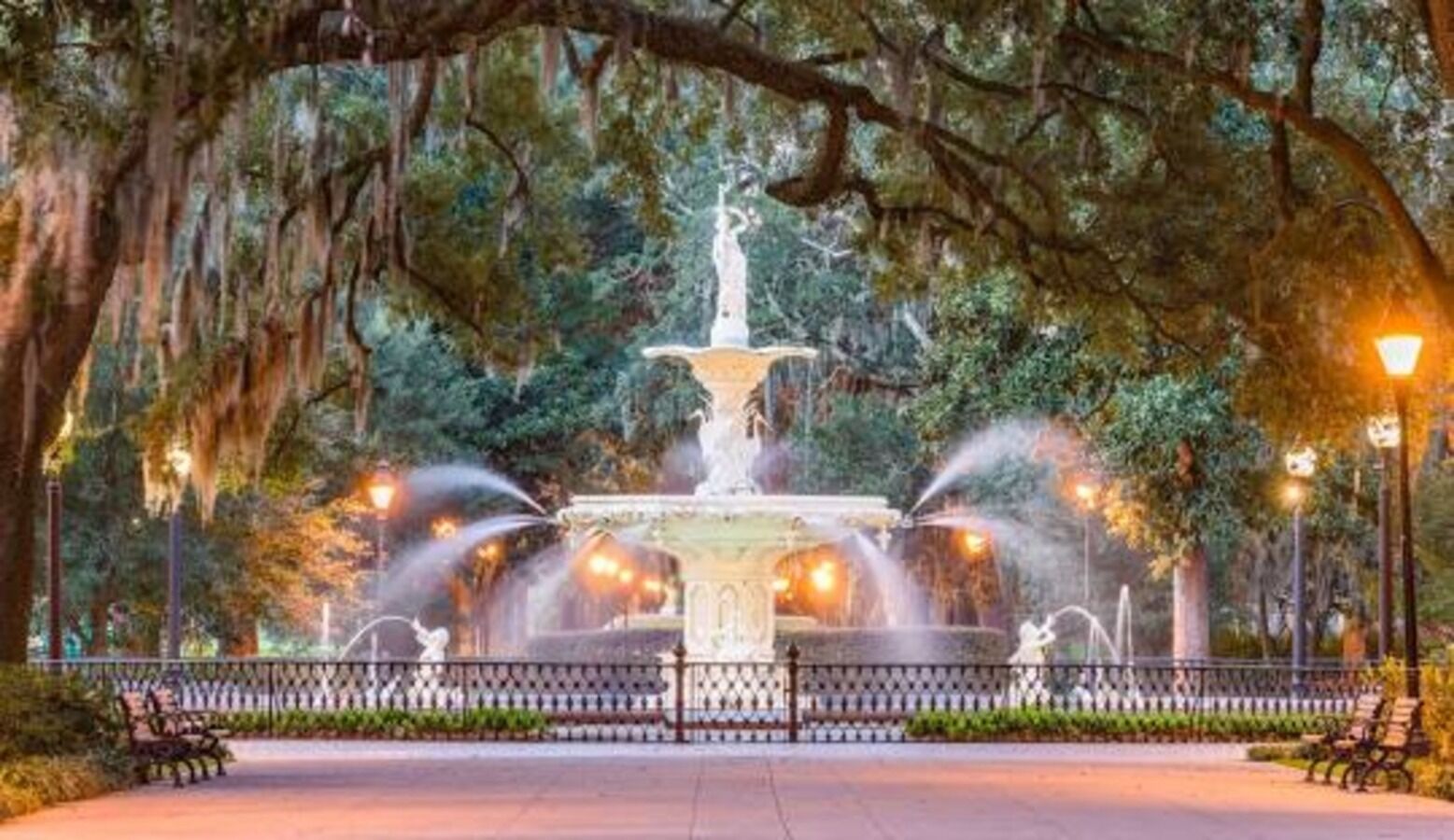 A park with a central fountain, surrounded by benches and a fence.