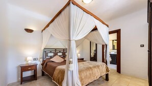 A four-poster canopy bed with a brown bedspread, a nightstand with a lamp, and a mirror on the wall. - CAN COSMI (Santa Eulalia del Río)