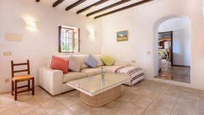 A living room with a sofa, a glass coffee table, a wooden chair, and a window with blinds. - CAN COSMI (Santa Eulalia del Río)