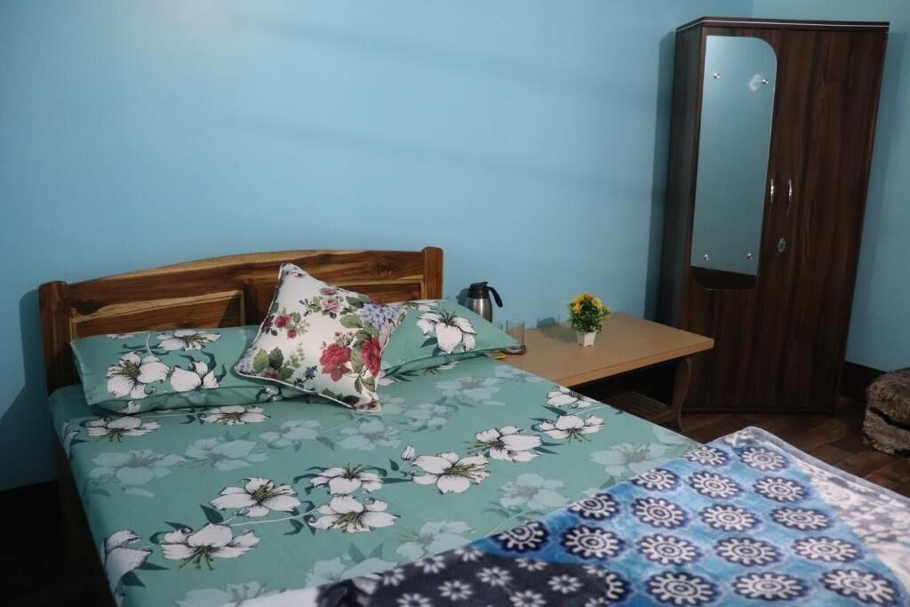 A bedroom with a bed, a wooden headboard, a nightstand with a lamp, a mirror, and a wardrobe.