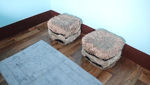 Two round, furry ottomans on a wooden floor next to a light blue rug.