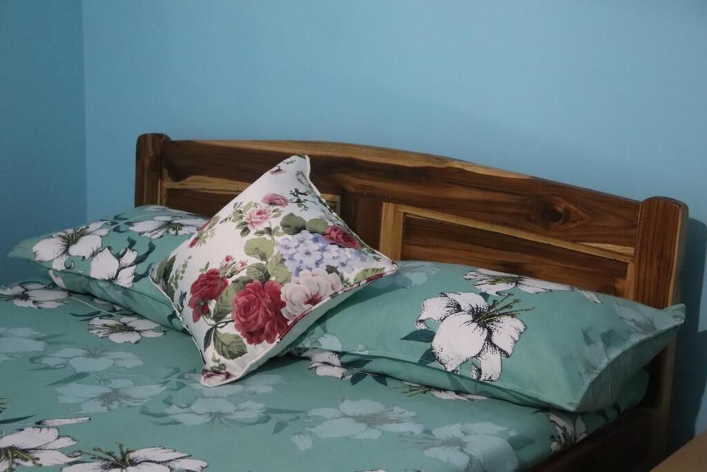 Una cama con una colcha estampada con flores y dos almohadas, una con diseño floral y la otra con motivos florales blancos.