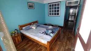A bedroom with a wooden bed, a small bedside table, a window, and a door leading to a bathroom.